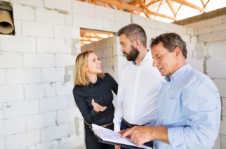 Young couple with architect or civil engineer looking at plans of their new house, discussing issues at the construction site.